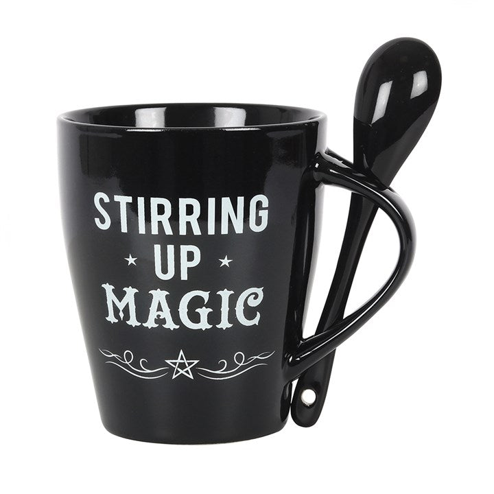 A black mug with a matching black spoon inserted into the handle, with white "Stirring up Magic", swirls and pentagram designs 