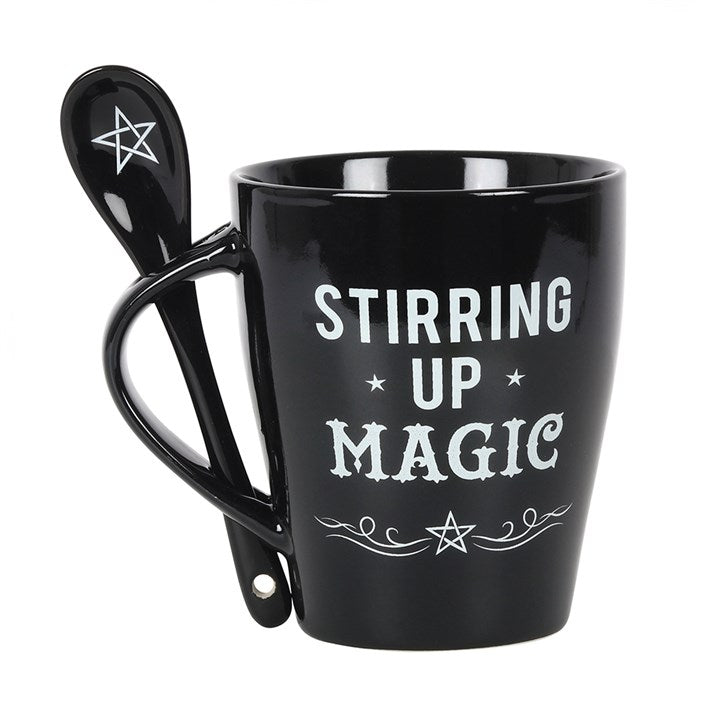 A black mug with a matching black spoon inserted into the handle, with white "Stirring up Magic", swirls and pentagram designs 