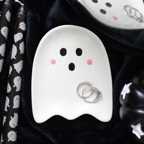 Ghost-shaped trinket dish with rings on a black surface with ghost patterns