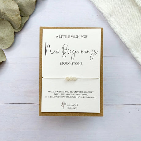Moonstone wish bracelet tied on a card with the text 'A little wish for New Beginnings' placed on a wooden surface with a neutral background.
