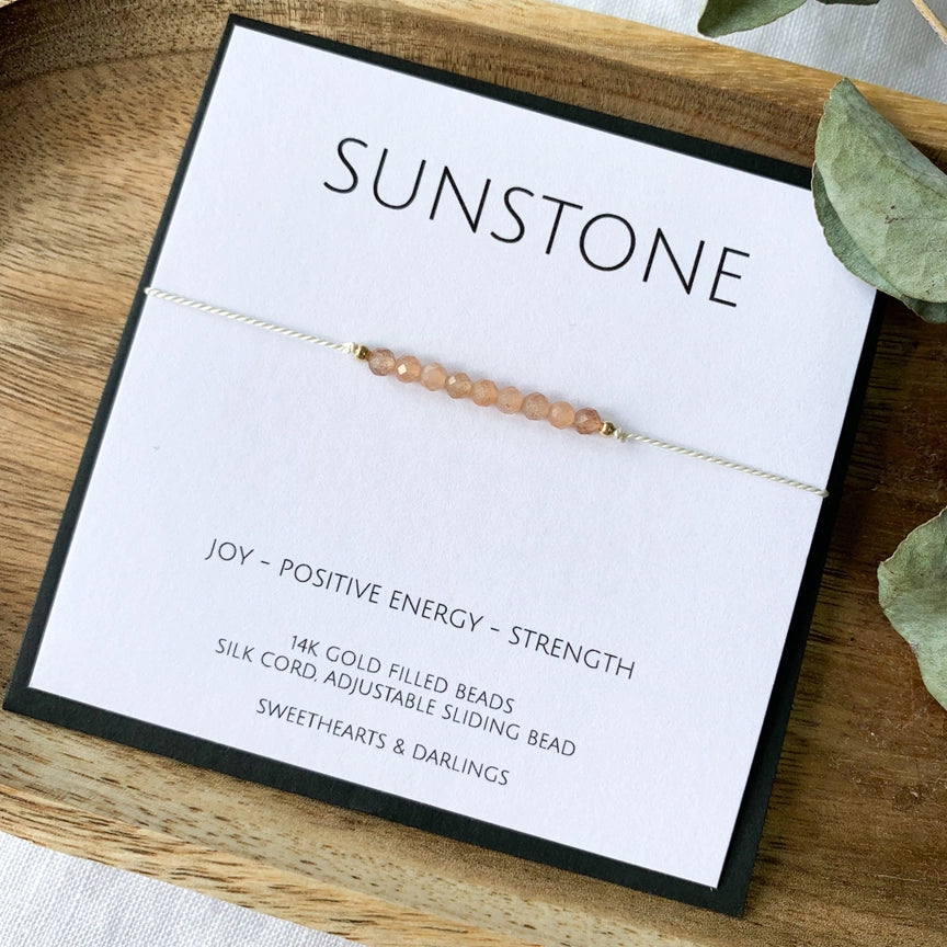 A Sunstone silk bracelet with beads approximately 3mm in size, displayed on a wooden tray alongside a keepsake card that reads 'Sunstone - JOY - POSITIVE ENERGY - STRENGTH'