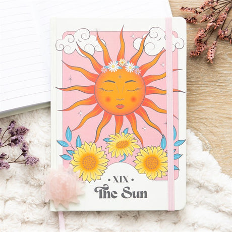 A5 notebook with a celestial design featuring a sun and flowers on the cover, placed on a desk with decorative elements around.