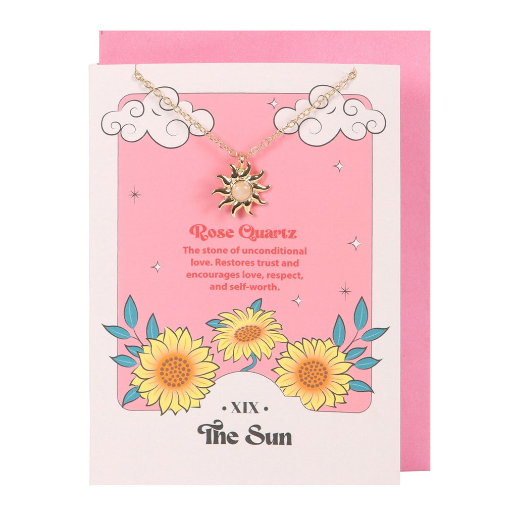 A stainless steel necklace with a sun pendant and a rose quartz crystal, displayed on a pink greeting card with tarot card designs and a pink envelope.