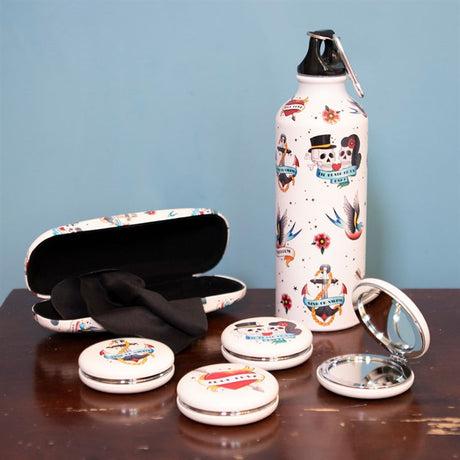 Old school tattoo themed accessories including a water bottle, open glasses cases and four compact mirrors on a wooden surface. 