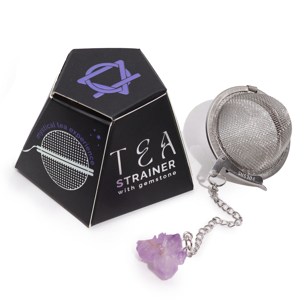 A metal tea strainer which has an amethyst crystal on a chain is placed next to its black box on a white surface 