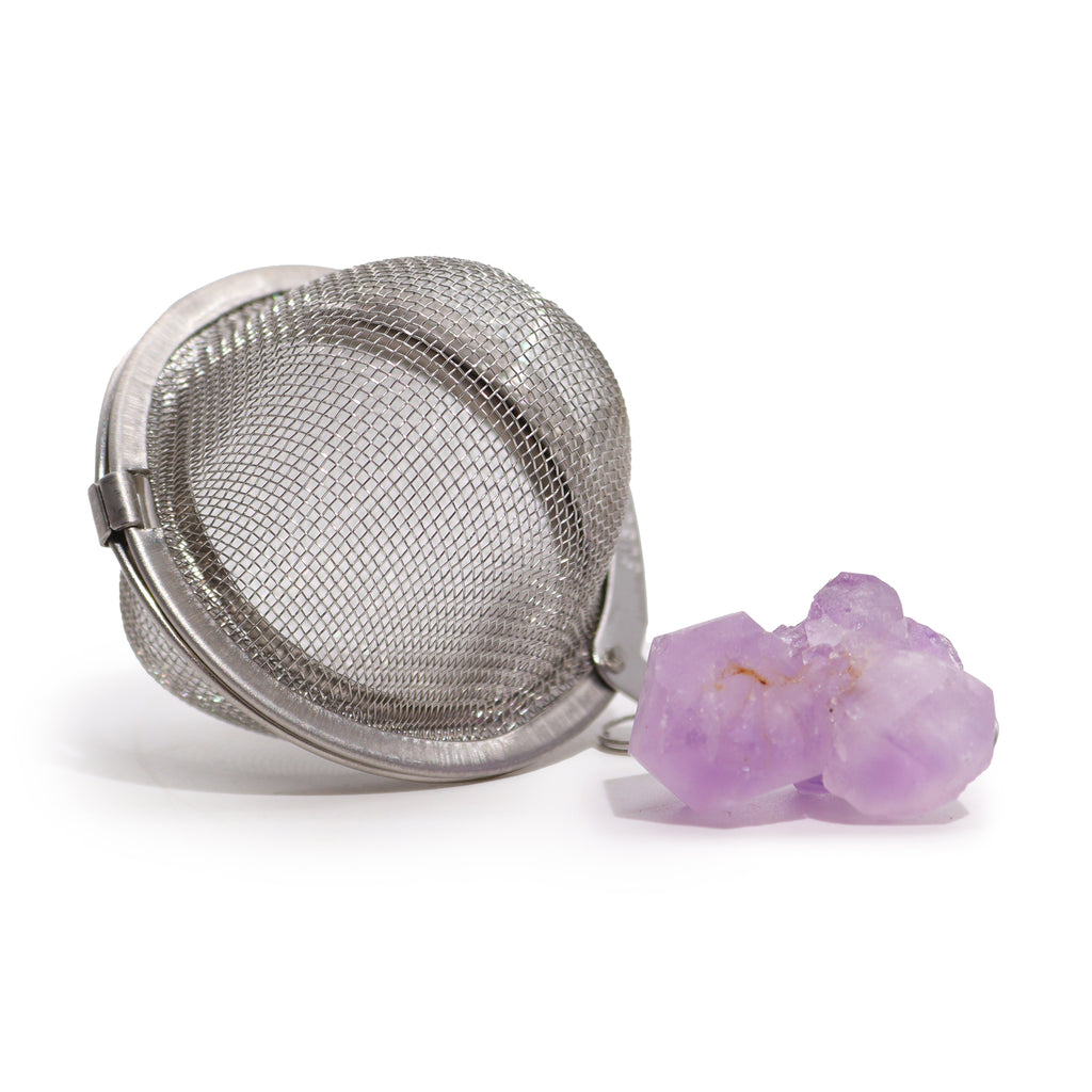 A metal tea strainer which has an amethyst crystal on a chain is on a white surface 