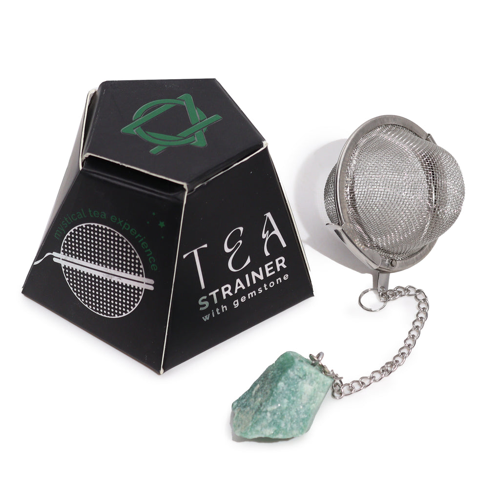 A metal tea strainer which has a green aventurine crystal on a chain is next to its black box, on a white surface 
