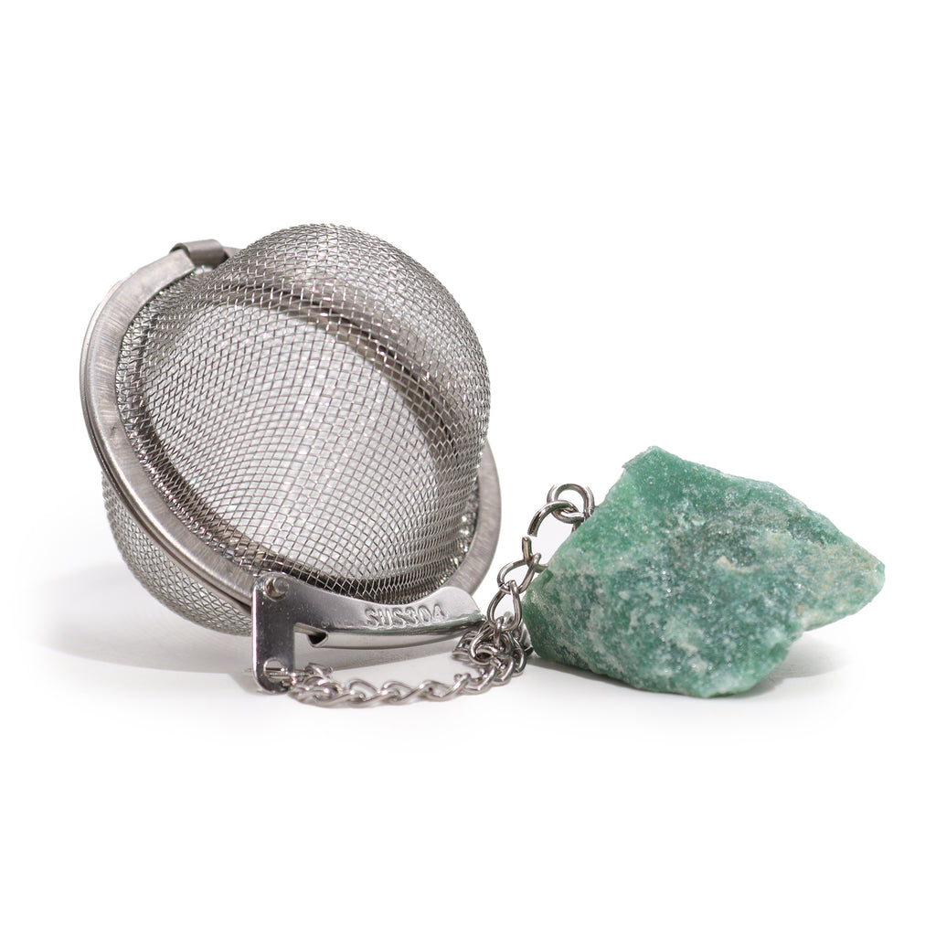 A metal tea strainer which has a green aventurine crystal on a chain is on a white surface 