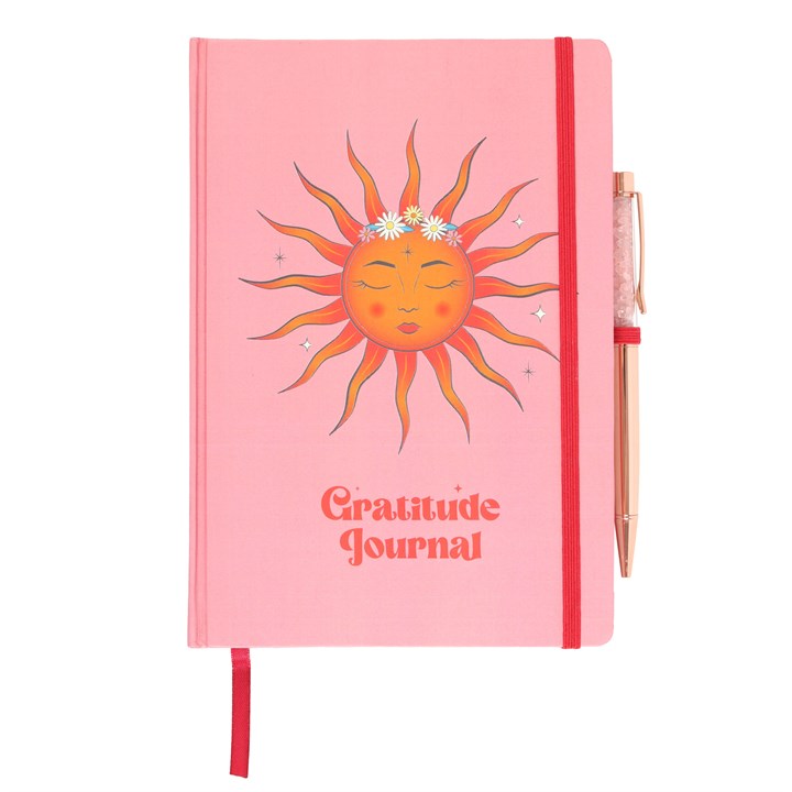A pink 'Gratitude Journal' with a sun and floral design on the cover, accompanied by a rose quartz pen.