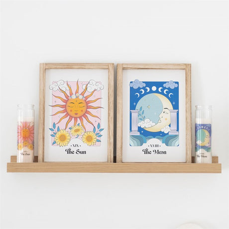 A pink and yellow sun themed tube candle and matching artwork sit beside a blue moon themed artwork and tube candle on a wooden shelf against a white wall.