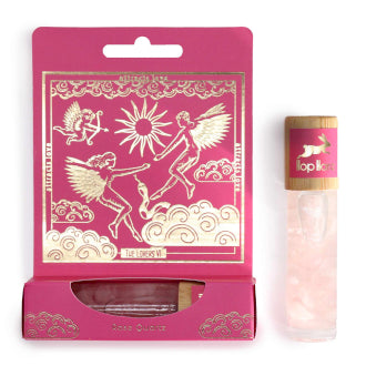 An essential oil gemstone roll-on with a wooden cap by Hop Hare, accompanied by pink tarot card with gold illustrations.