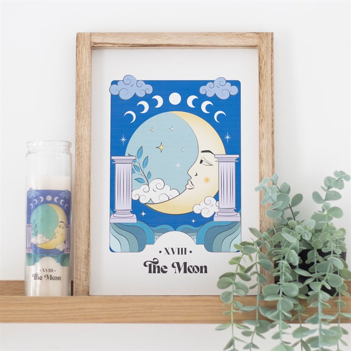 A blue moon themed artwork and tube candle on a wooden shelf against a white wall.