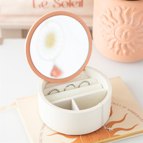 Jewellery box with a mirror lid containing rings and a necklace on a light background.