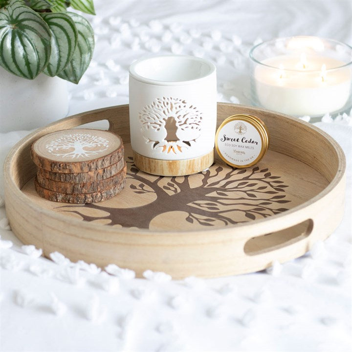 Four piled wooden coasters with a white tree of life motif on a tree of life tray, next to a white tree of life tea light holder and a wax melt.