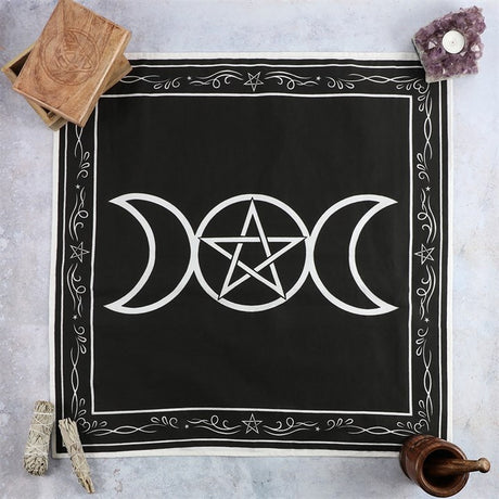 A black cotton altar cloth with a white printed design featuring a triple moon and pentagram, displayed on a flat surface with a wooden box and incense in the background.