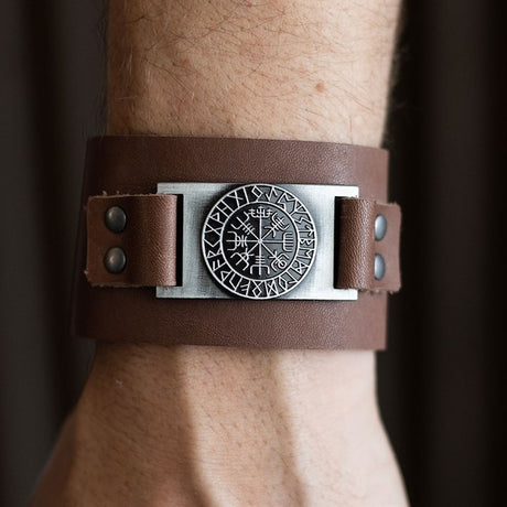 Brown leather bracelet with a Viking emblem on a wrist against a dark background