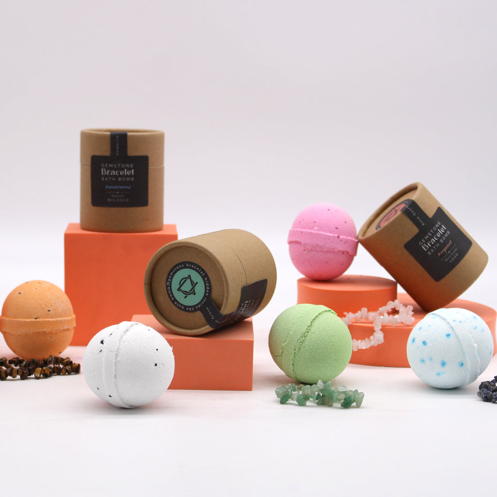 A collection of colourful bathbombs and their brown cylinder containers and crystal bracelets