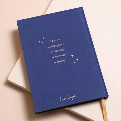 A navy blue journal with a gold detail on the cover, featuring "Fall in love with the process of becoming the best version of yourself" with a gold page edge.