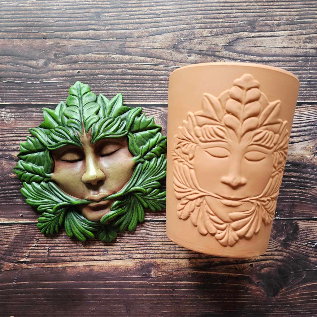 A "Green Goddess" green man themed plaque lays next to the same designed terracotta plant pot