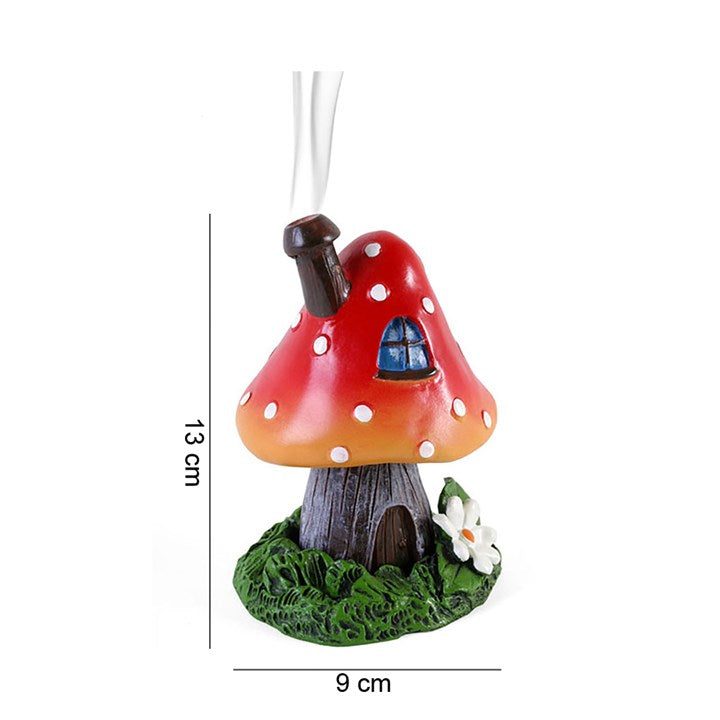 A red and orange toadstool-shaped incense burner with a house and chimney design, on a green base, intended for burning incense cones.