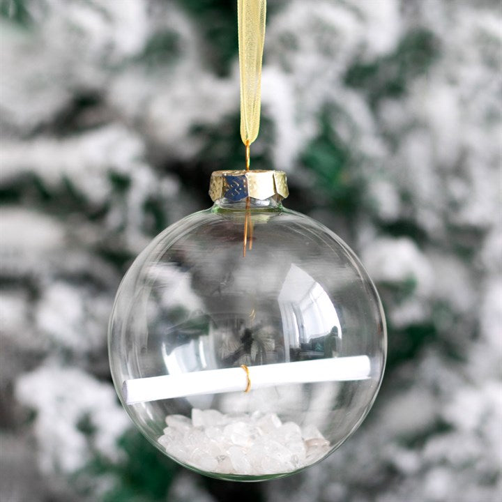 A glass bauble on a gold string with a scroll of paper inside along with crystals. 