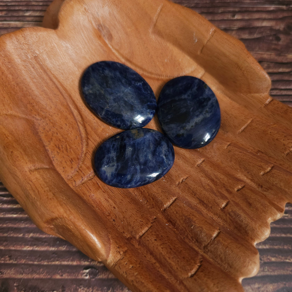 Three blue polished crystal thumbstones resting on a wooden surface