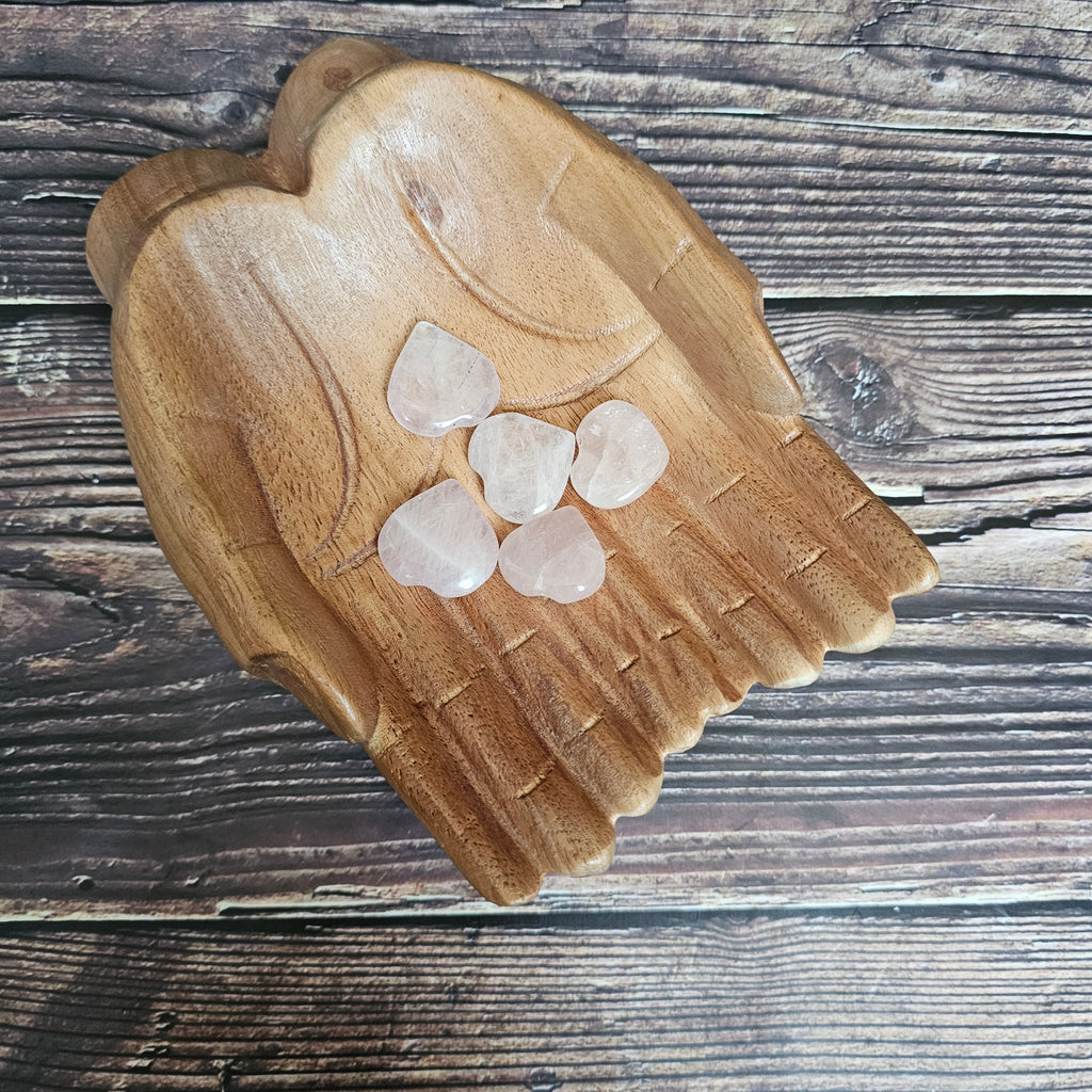 A collection of polished, carved crystal hearts in pink, placed on a wooden surface.