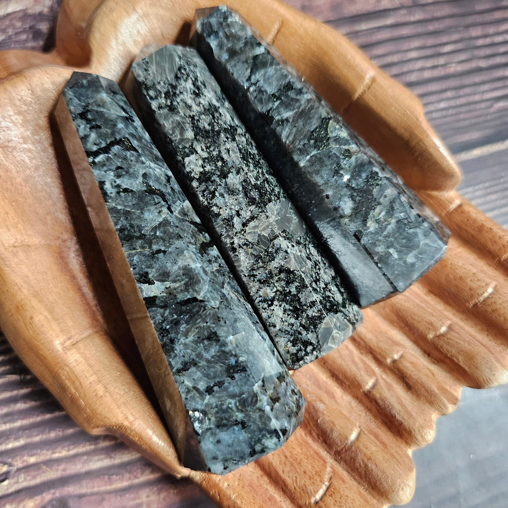 Three Larvikite obelisks laid down on a pair of wooden hands