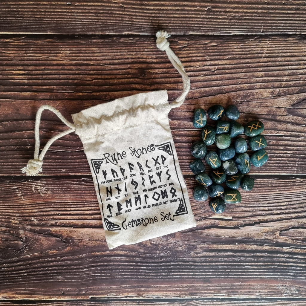 A collection of Moss Agate rune stones displayed on a wooden surface with a beige coloured "Rune Stones" bag