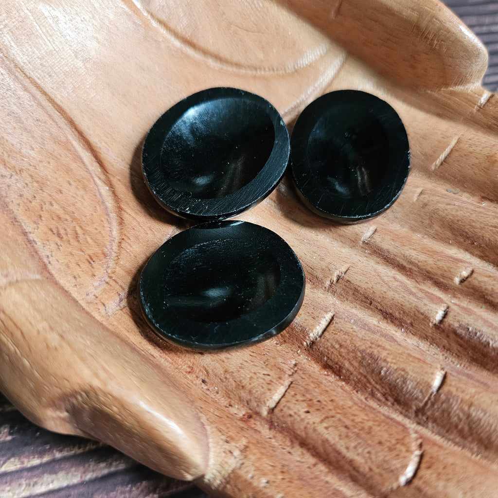 Three black polished crystal thumbstones resting on a wooden surface