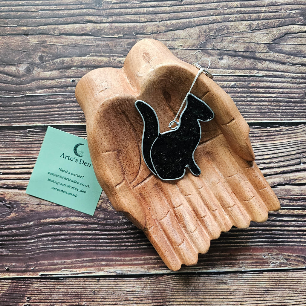 A black sparkly cat suncatcher on a pair of wooden hands. 