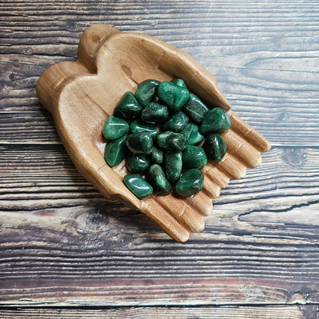 A collection of dark green Aventurine tumblestones placed on a wooden hands-shaped dish, set against a wooden background.