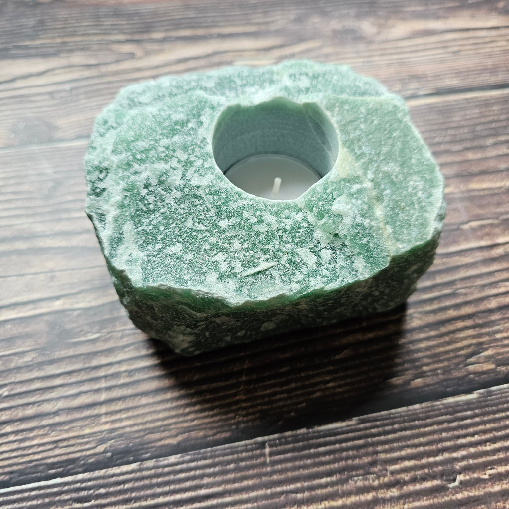 A chunky rough, green aventurine stone tealight holder placed on a wooden surface.