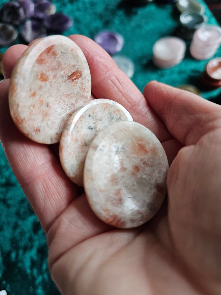 Three sunstone polished crystal thumbstones being held in a hand