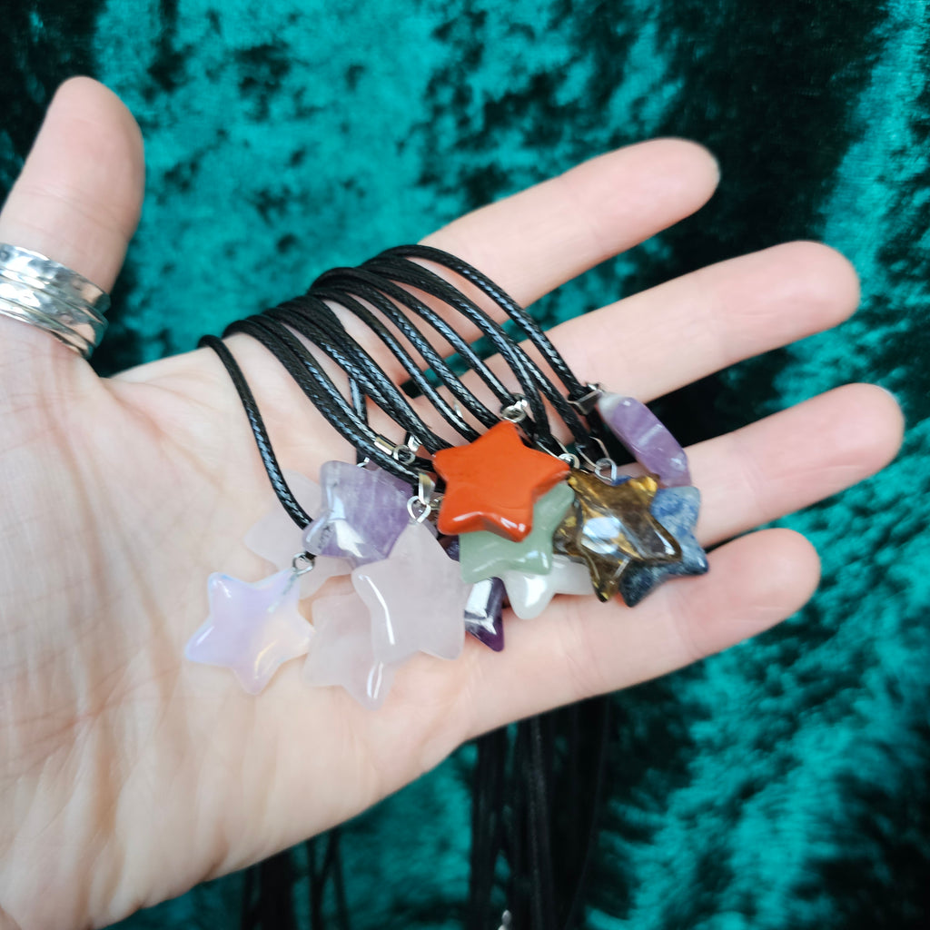 Several star-shaped crystal pendants in various colours held in someone's hand, with a black cord.