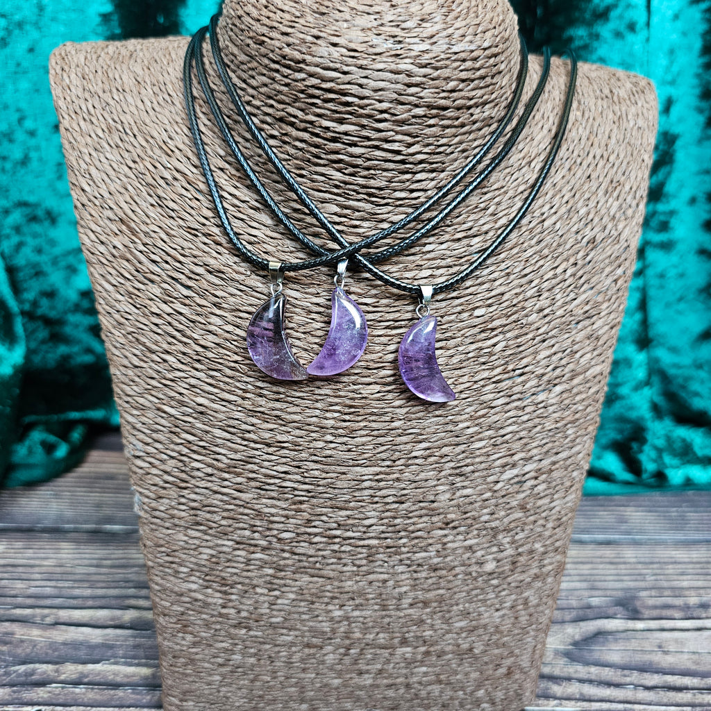 Three crescent moon shaped crystal pendants on a black cord displayed on a mannequin 