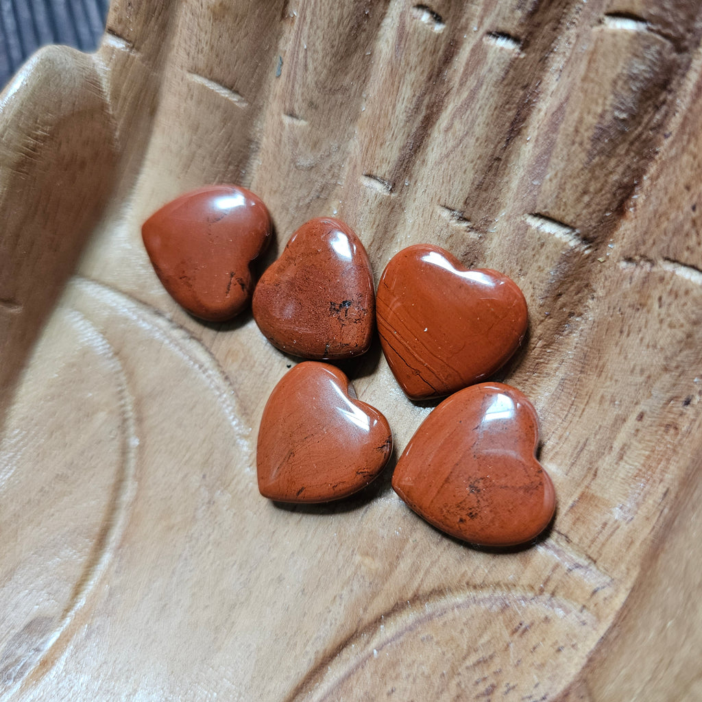 A collection of polished, carved crystal hearts in various shades of red, placed on a wooden surface.