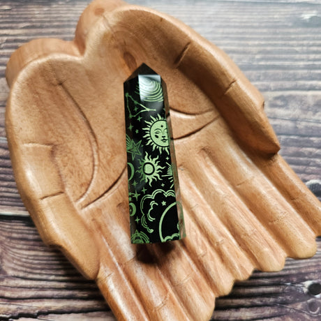A Black Obsidian Generator with celestial designs displayed on a wooden hand-shaped tray.