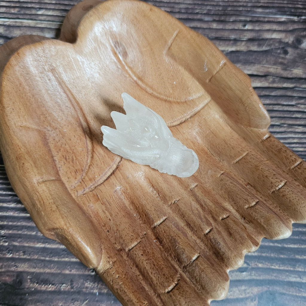 A clear quartz crystal dragon skull figurine, placed on a wooden surface.