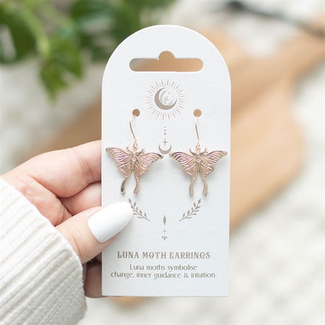 A pair of dangling light luna moth earrings displayed on a backing card 