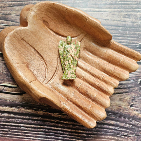 A carved crystal angel figurine placed inside a wooden hand-shaped bowl.