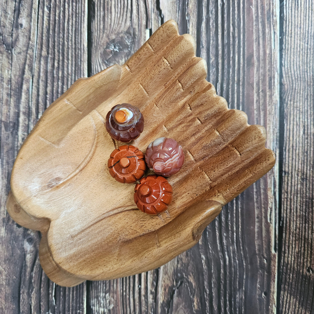 Four carved crystal pumpkins being held in a pair of wooden hands