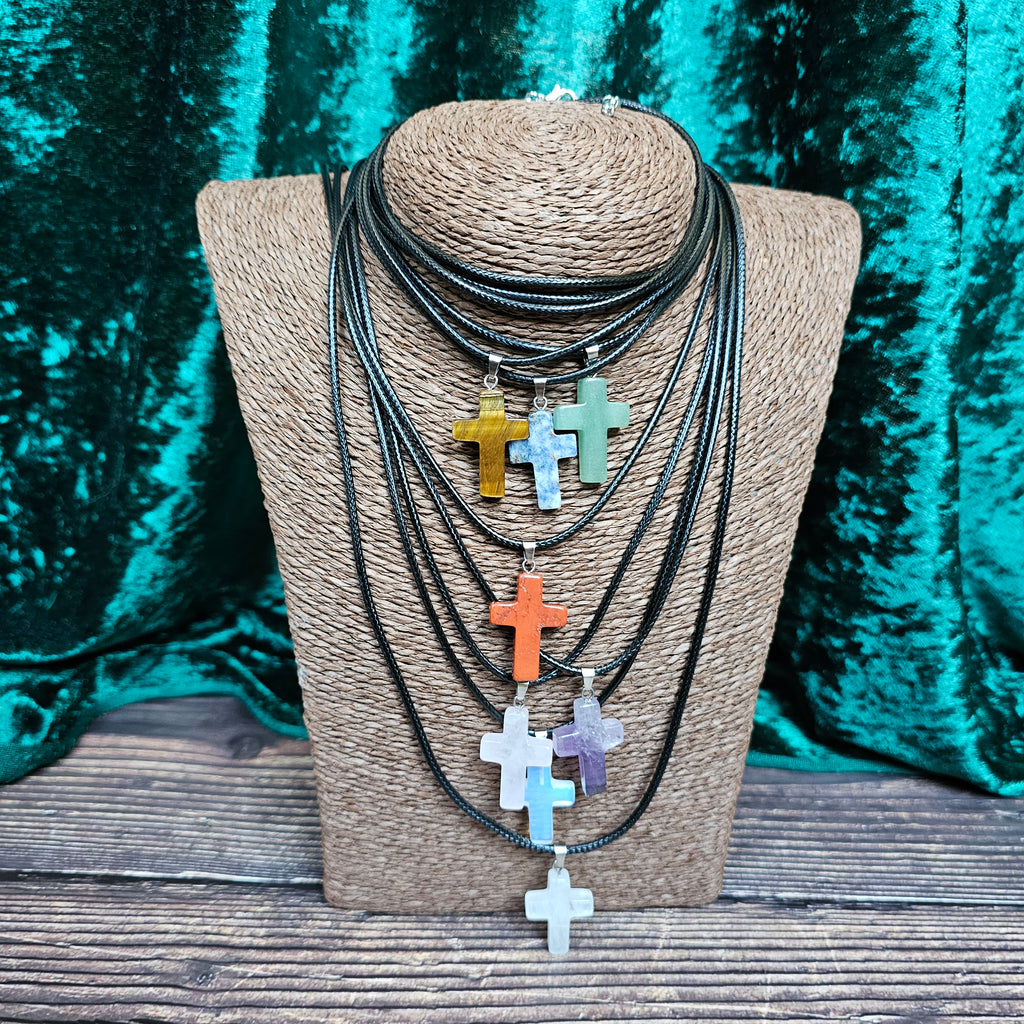 Several cross-shaped crystal pendants with a black cord necklace displayed on a mannequin.