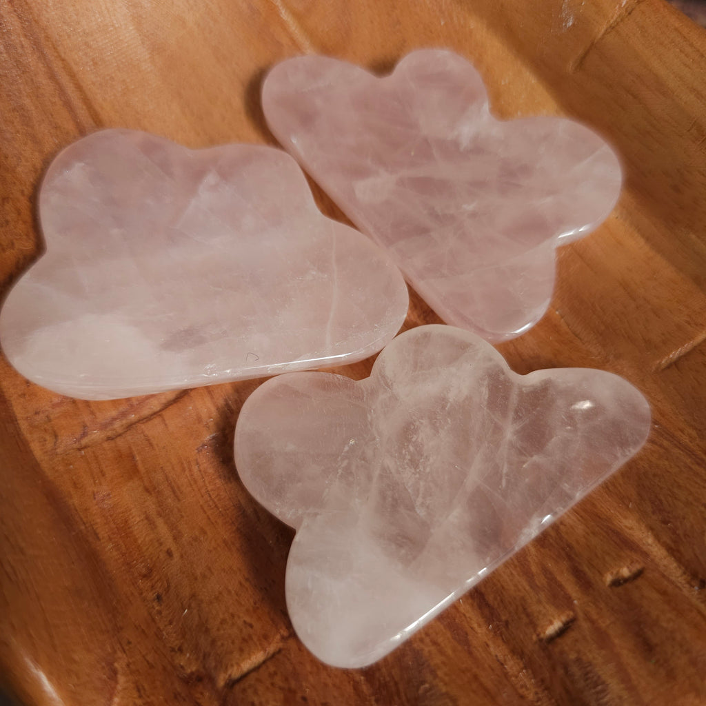 Carved rose quartz crystals shaped like clouds, placed on a wooden surface.