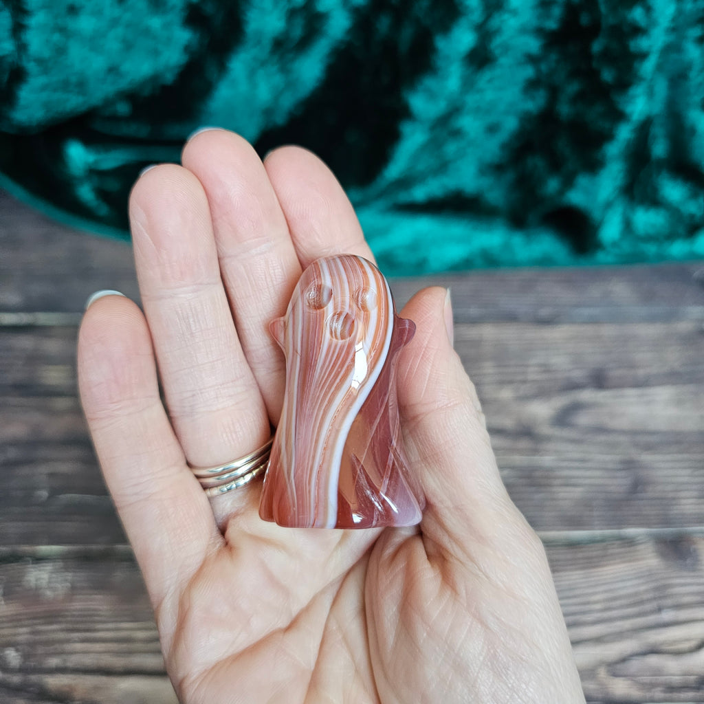 The front of a Carnelian carved crystal ghost held in a person's hand