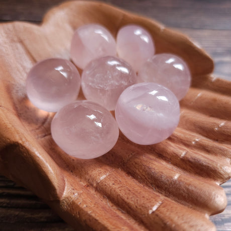 A collection of round rose quartz tumblestones placed on a wooden dish.