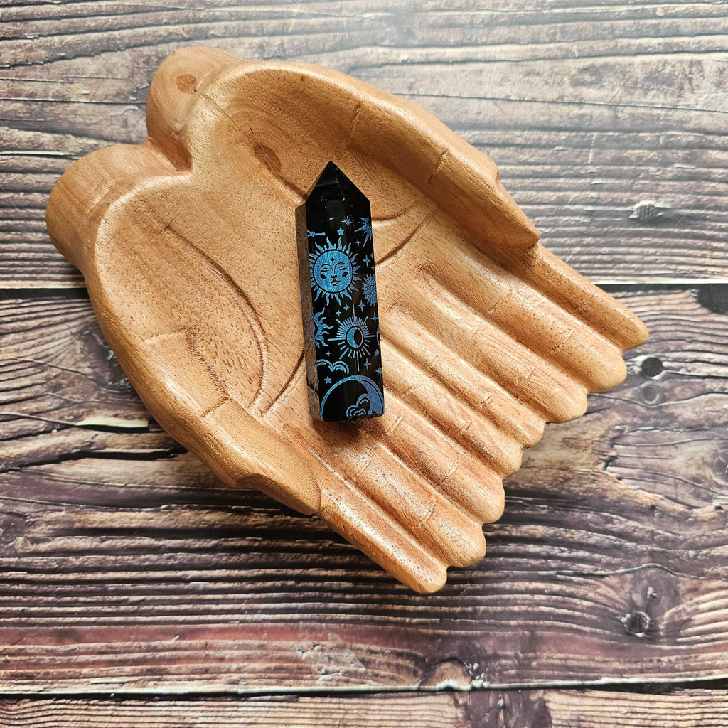 A Black Obsidian Generator with celestial designs displayed on a wooden hand-shaped tray.
