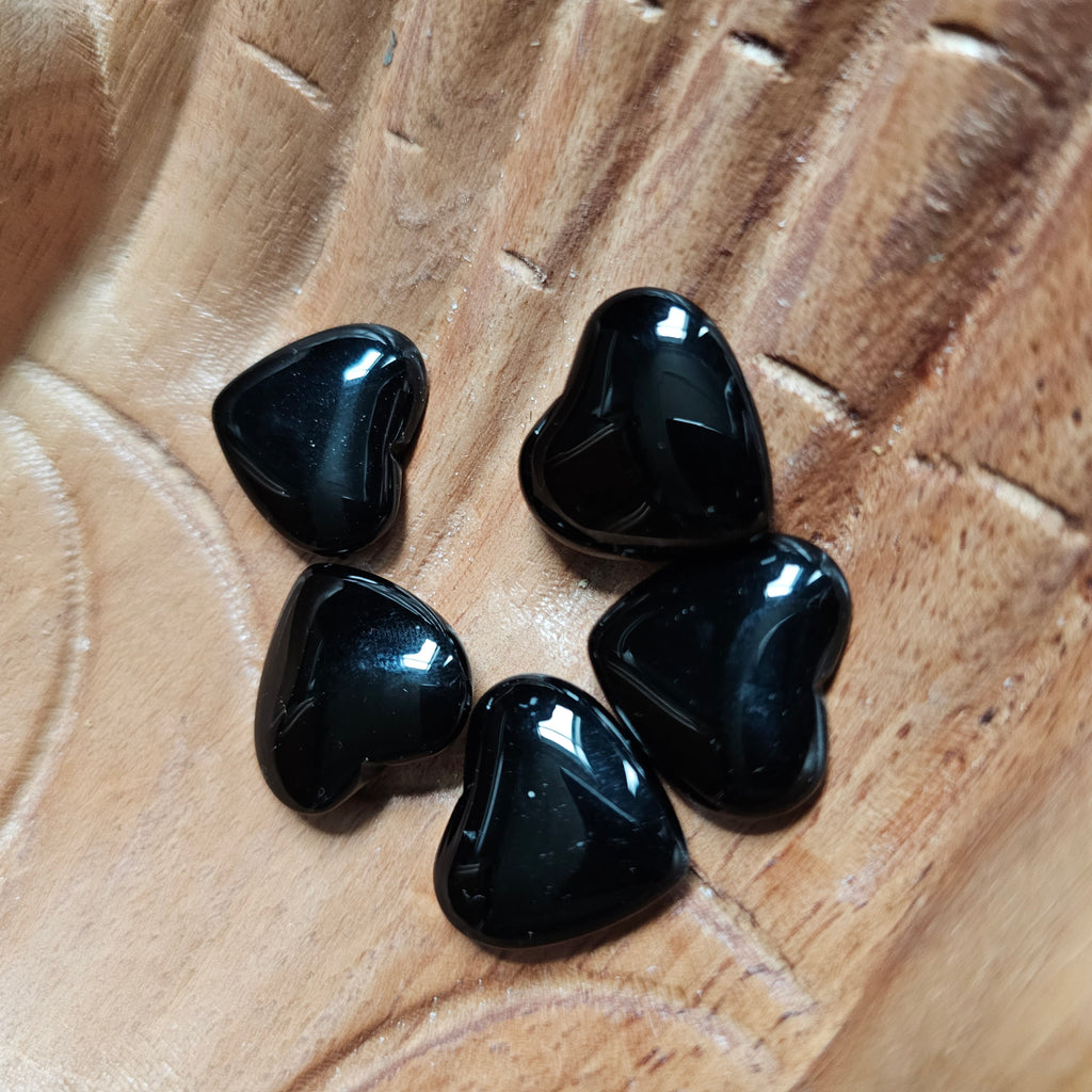 A collection of polished, black carved crystal hearts placed on a wooden surface.