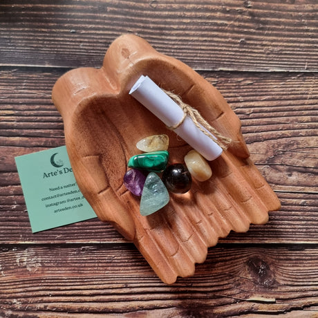 A collection of polished crystals and a scroll of paper displayed in a pair of wooden hands, with a business card that reads 'Arte's Den'.