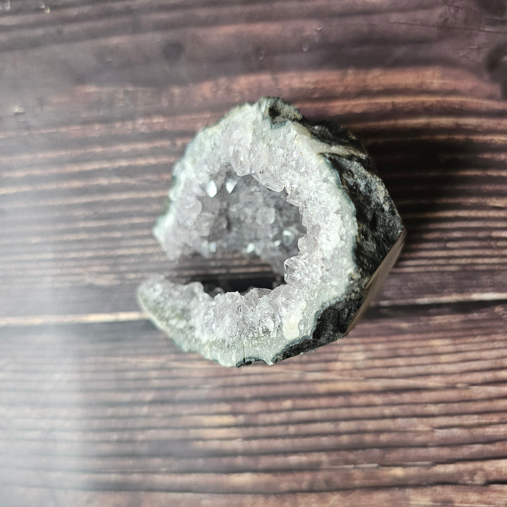 A rough, opaque purple Amethyst crystal in a standing cluster shape on a wooden surface.